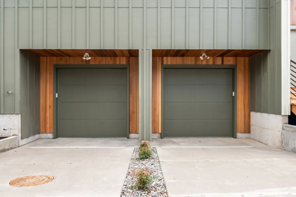 This image features a contemporary exterior view, highlighting two garage doors, wood paneling, and a stone pathway—elements that underscore off-street parking and convenience. The scene feels functional and modern, reinforcing ease of arrival and departure for busy travelers.