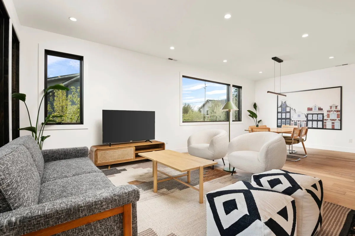 The image showcases a bright, stylish living and dining area featuring a plush sofa, a modern dining table, a large TV, and tasteful Scandinavian-inspired art. The space is designed for comfort, perfect for unwinding with a movie, sharing meals, or enjoying game night with friends and family.