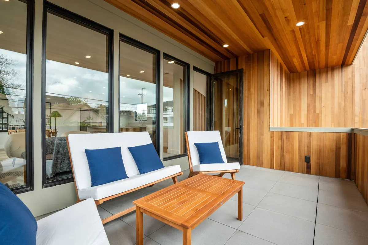 A calm and welcoming exterior space with a wooden ceiling and modern seating, surrounded by glass windows and a wooden table. The patio enjoys sunset views and soft morning light, providing a perfect location for unwinding or socializing at different times of day.