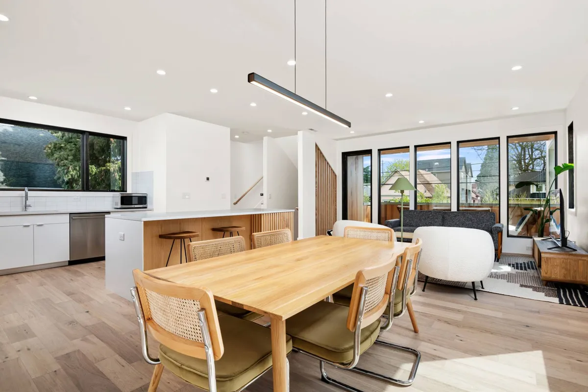 A spacious open-plan kitchen and dining area flooded with natural light from large windows. The scene is set for group meals, with a welcoming and casual vibe that encourages gathering and sharing stories.