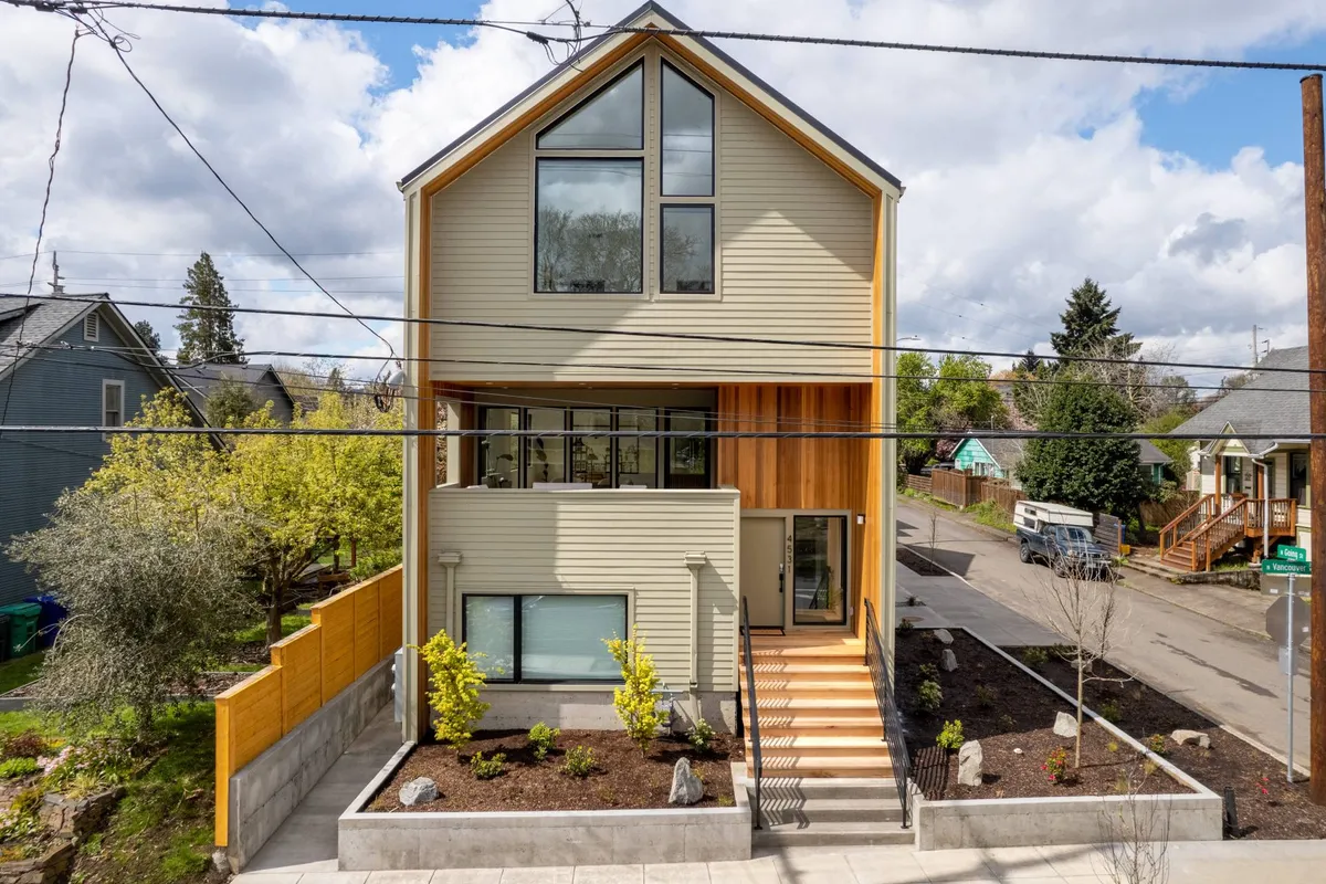 A lively, inviting exterior scene that showcases the property's modern architecture, expansive windows, wood elements, and a well-maintained front yard where a family gathering takes place. Children play in the yard while neighbors chat on the porch, radiating a sense of friendly community and active outdoor living.