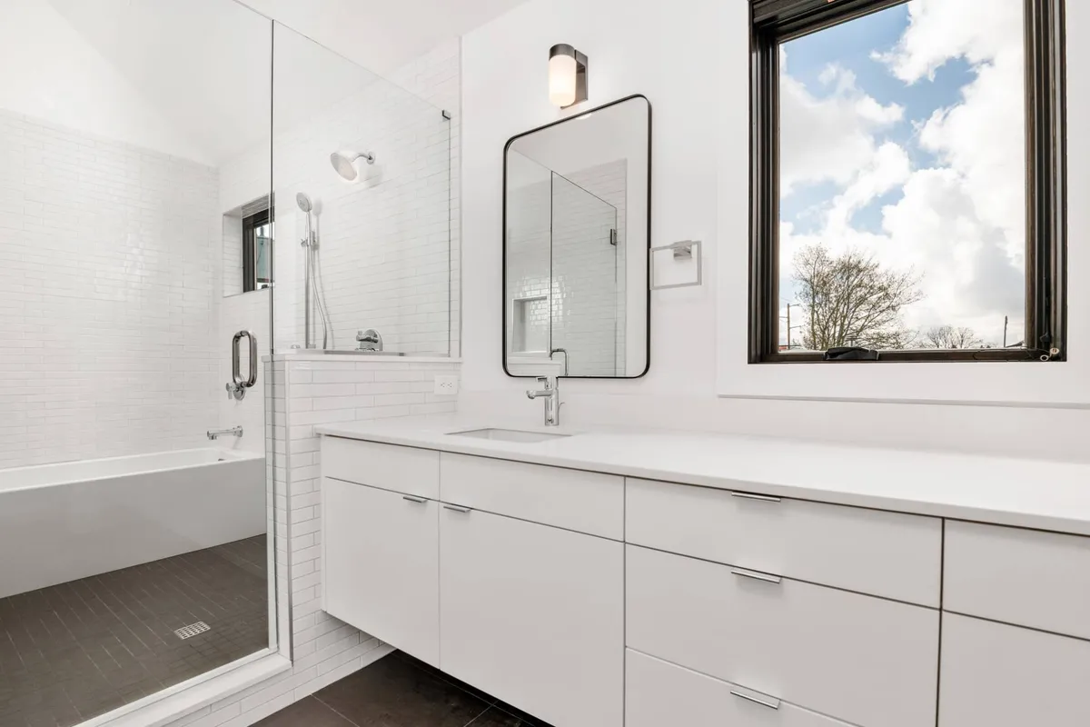 A serene bathroom highlighted by a spacious shower area, vanity with a large mirror, and a window that lets in gentle daylight. The neutral palette and clean design evoke a spa-like ambiance, perfect for morning routines or evening relaxation.