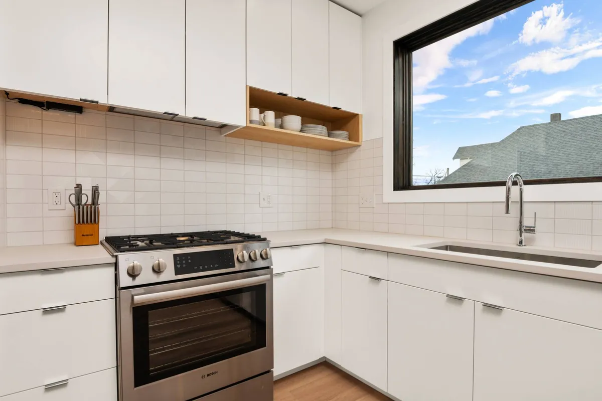 A bright, functional kitchen featuring a stainless steel oven, pristine white cabinetry, and a large window. The scene suggests easy meal prep with modern appliances, inviting families or groups to gather and enjoy home-cooked meals.